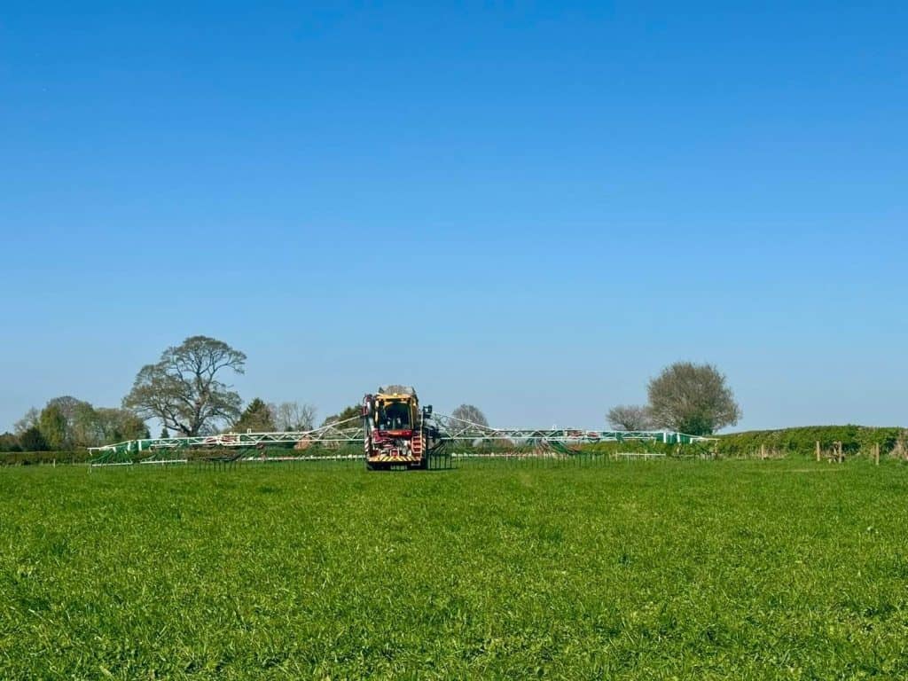 Agricultural machine spraying green field, clear sky