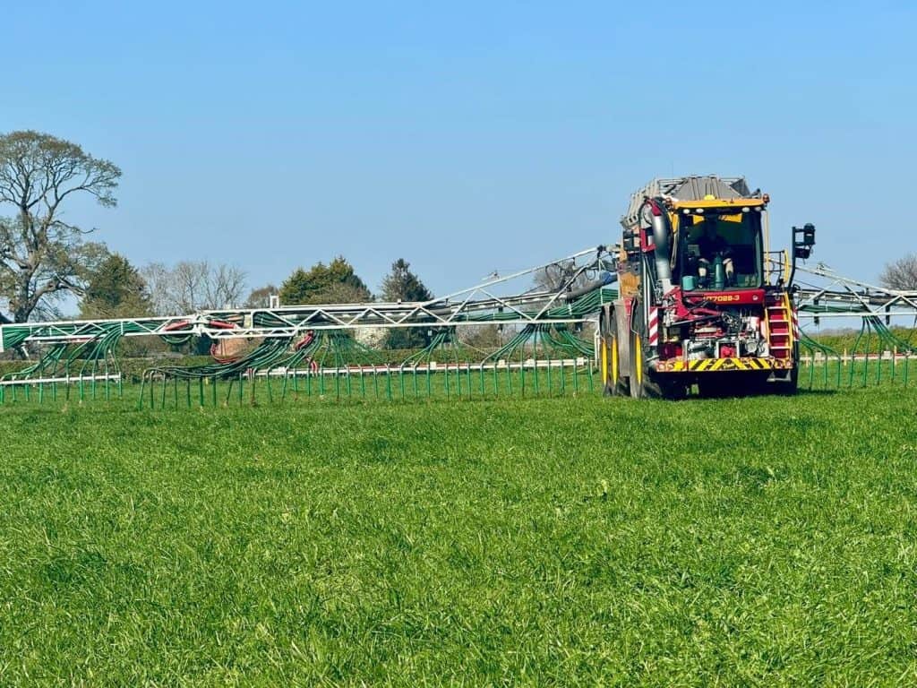 Farm machinery fertilizing a green field under blue sky.